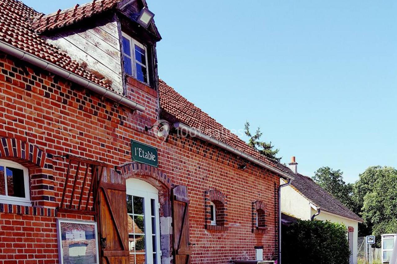 Façade en briques rouges d'un bâtiment rural avec des volets en bois et une enseigne indiquant ’L'Itable’.