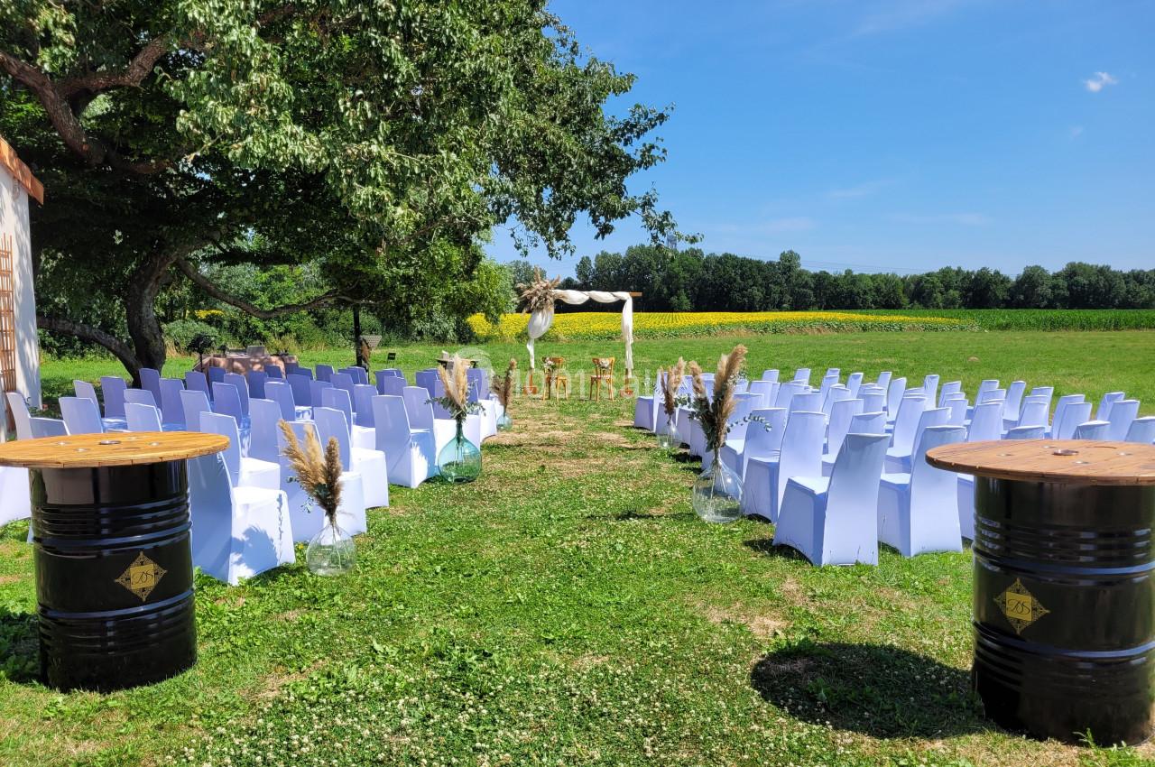 Chaises blanches alignées en extérieur face à une arche décorée, entourées de verdure sous un ciel dégagé.