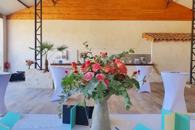 Bouquet de fleurs blanches et vertes au premier plan, avec des chaises disposées en extérieur sous un grand arbre.