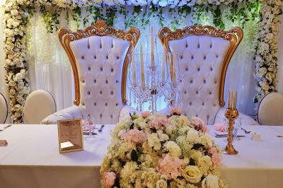 Bouquet de fleurs blanches et vertes au premier plan, avec des chaises disposées en extérieur sous un grand arbre.