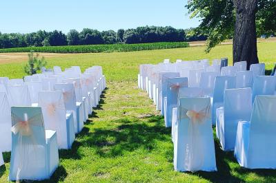 Bouquet de fleurs blanches et vertes au premier plan, avec des chaises disposées en extérieur sous un grand arbre.