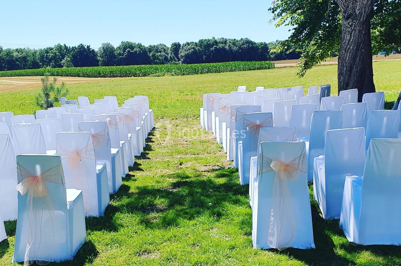 Chaises blanches décorées de rubans roses disposées en rangées sur une pelouse, prêtes pour une cérémonie en extérieur.