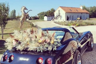 Bouquet de fleurs blanches et vertes au premier plan, avec des chaises disposées en extérieur sous un grand arbre.