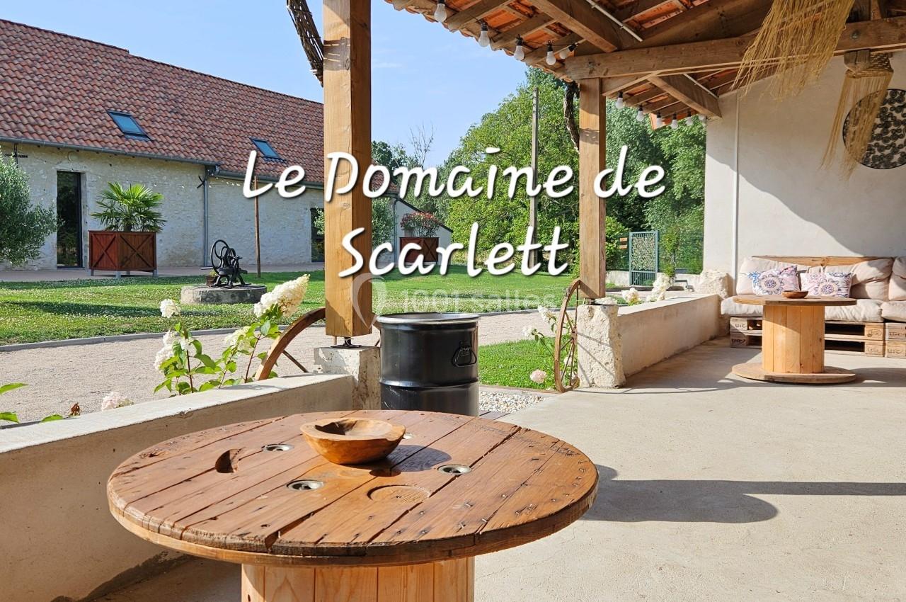 Table basse en bois sous une terrasse couverte, avec vue sur un jardin et des bâtiments en arrière-plan.