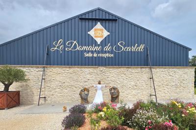 Bouquet de fleurs blanches et vertes au premier plan, avec des chaises disposées en extérieur sous un grand arbre.
