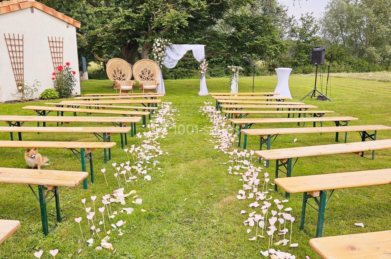 Allée centrale bordée de bancs en bois, décorée de pétales, menant à une arche florale pour une cérémonie en plein air.