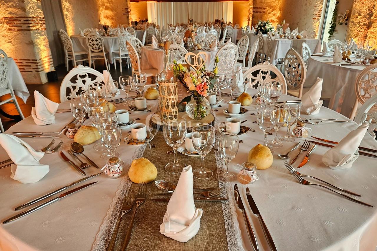 Salle de réception avec tables rondes élégamment dressées, nappes blanches, vaisselle raffinée et décoration florale.