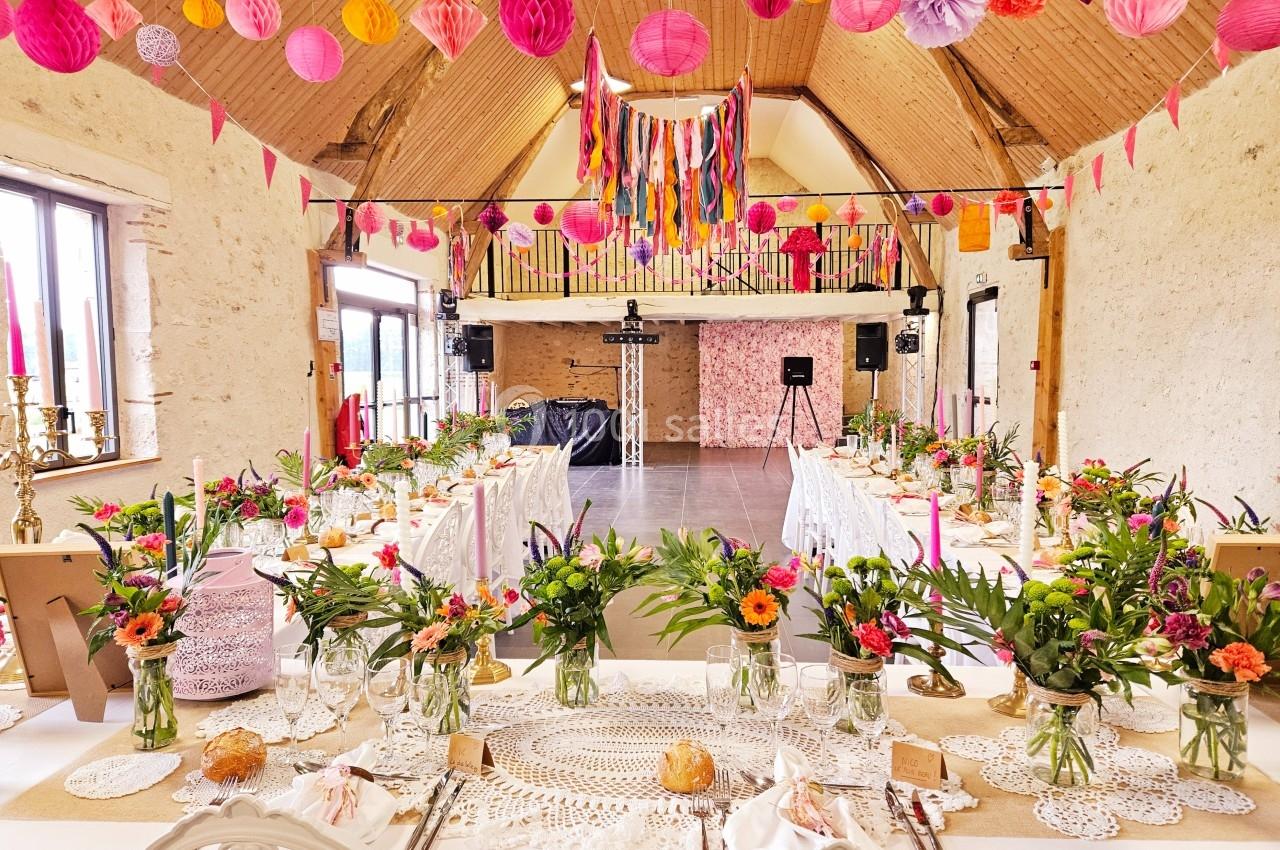 Salle de réception décorée avec des guirlandes colorées, des fleurs et des tables dressées pour un événement festif.