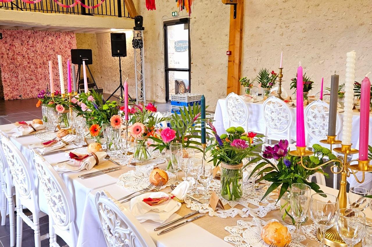 Grande table décorée pour un événement, ornée de fleurs colorées, bougies et guirlandes dans une salle lumineuse.