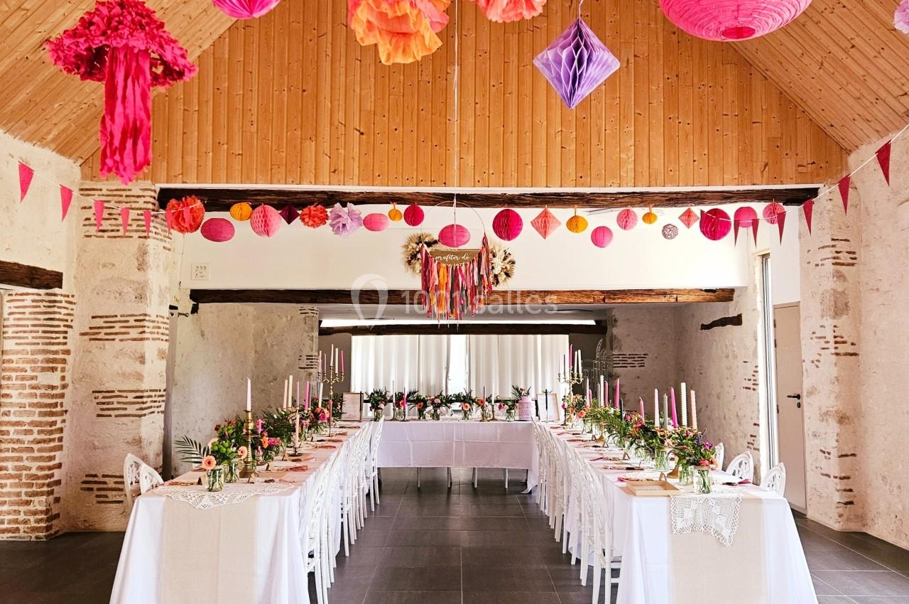 Salle de réception décorée avec des guirlandes colorées, des tables dressées et des compositions florales.
