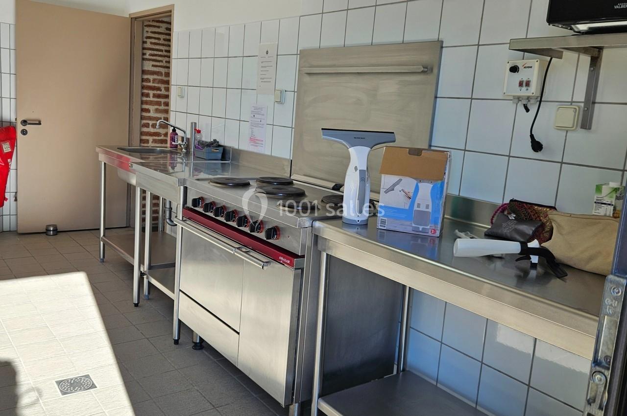 Cuisine professionnelle avec plaques de cuisson, hotte, plans de travail en inox et carrelage mural blanc.