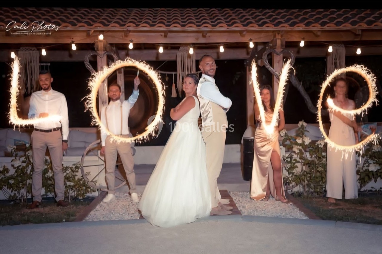 Un couple de mariés pose avec des invités formant le mot ’LOVE’ avec des cierges magiques allumés.