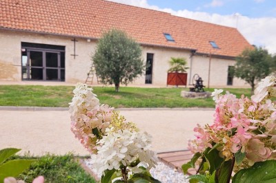 Bouquet de fleurs blanches et vertes au premier plan, avec des chaises disposées en extérieur sous un grand arbre.