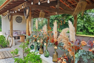 Bouquet de fleurs blanches et vertes au premier plan, avec des chaises disposées en extérieur sous un grand arbre.