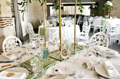 Bouquet de fleurs blanches et vertes au premier plan, avec des chaises disposées en extérieur sous un grand arbre.