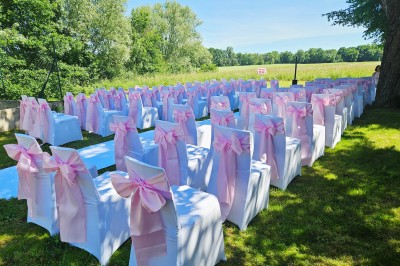 Un couple en tenue de mariage s'embrasse devant une arche décorée, dans un cadre champêtre en plein air.