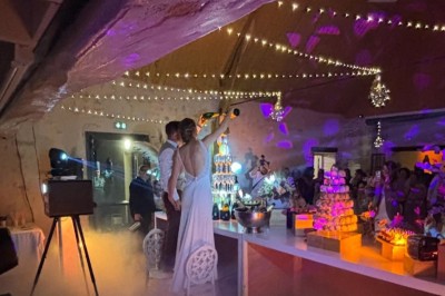 Un couple en tenue de mariage s'embrasse devant une arche décorée, dans un cadre champêtre en plein air.