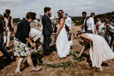 Un couple en tenue de mariage s'embrasse devant une arche décorée, dans un cadre champêtre en plein air.