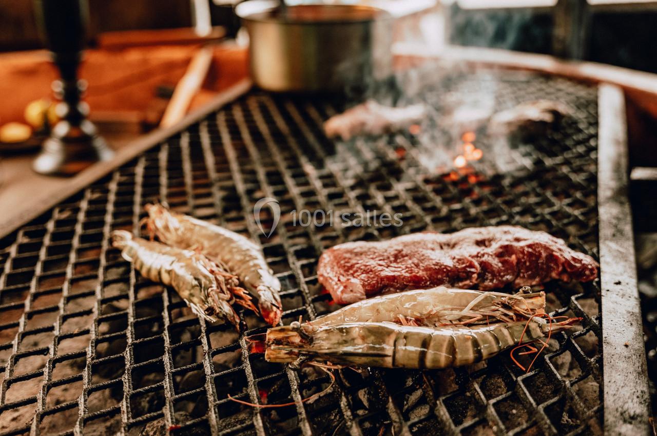Crevettes et morceaux de viande grillant sur un barbecue au charbon dans un cadre rustique.
