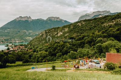 Terrasse extérieure animée avec tables, guirlandes lumineuses, vue sur un lac et montagnes en arrière-plan.