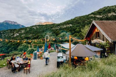 Terrasse extérieure animée avec tables, guirlandes lumineuses, vue sur un lac et montagnes en arrière-plan.