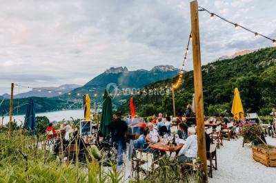 Terrasse extérieure animée avec tables, guirlandes lumineuses, vue sur un lac et montagnes en arrière-plan.
