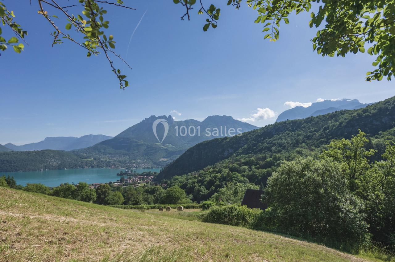 Paysage de montagne avec un lac turquoise, des collines verdoyantes et un ciel bleu dégagé.