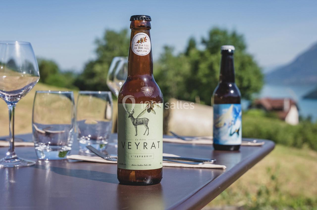 Bouteille de bière artisanale posée sur une table en extérieur avec vue sur un paysage naturel et des verres.