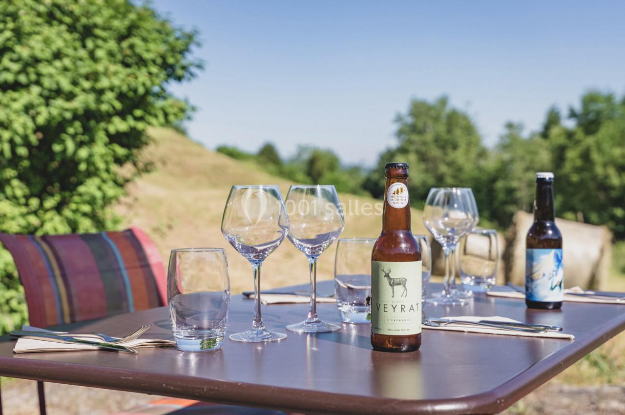 Table extérieure avec verres, couverts et bouteilles de bière, entourée de verdure sous un ciel dégagé.