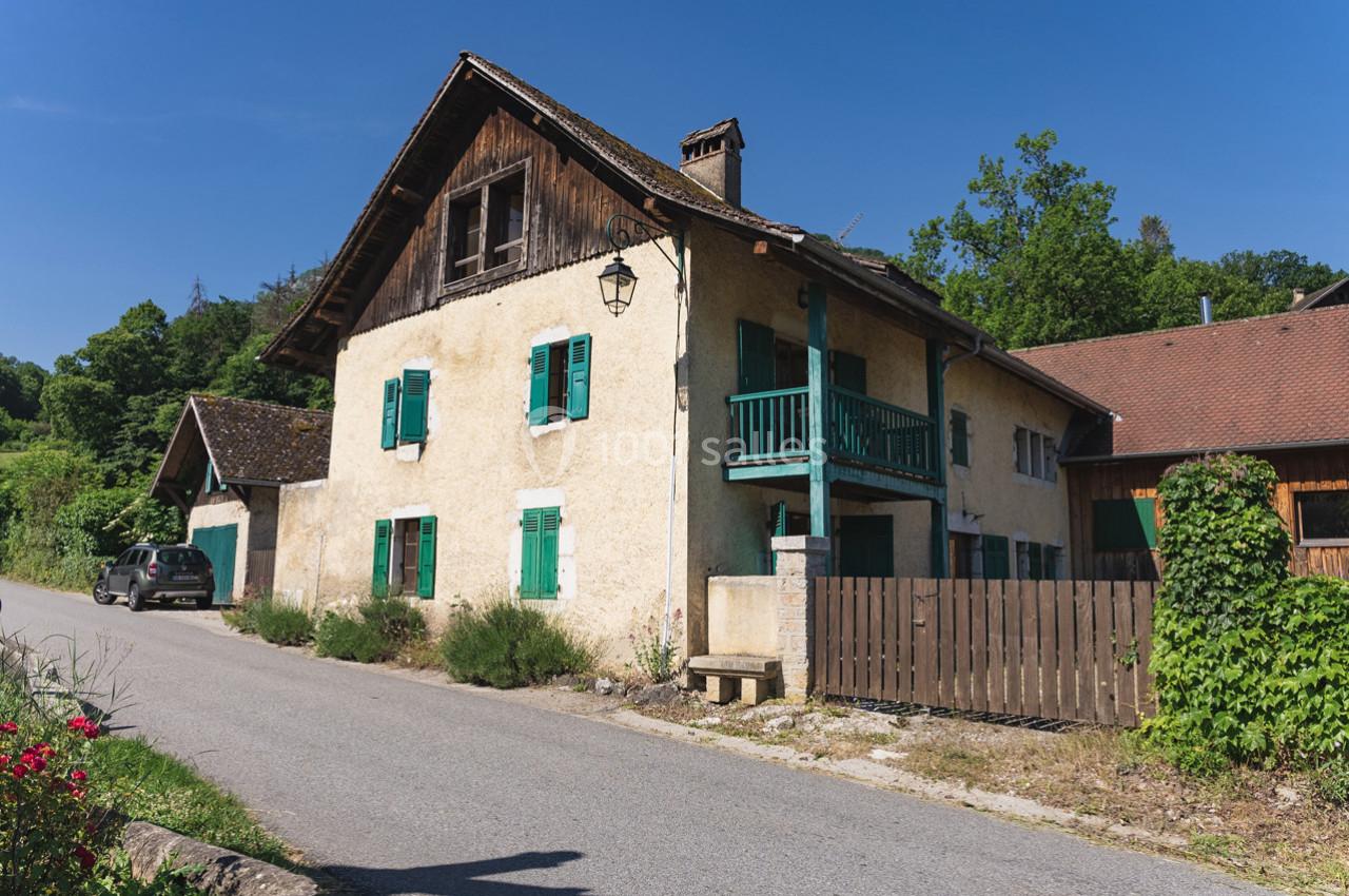 Maison traditionnelle avec façade en crépi jaune, volets verts, balcon en bois et toit en tuiles, située au bord d'une route.