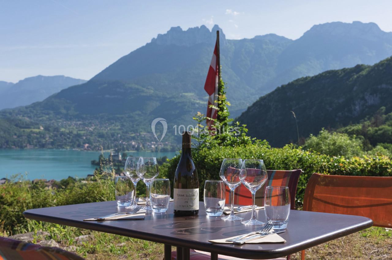 Table dressée avec des verres et une bouteille de vin, vue sur un lac entouré de montagnes et un drapeau suisse.