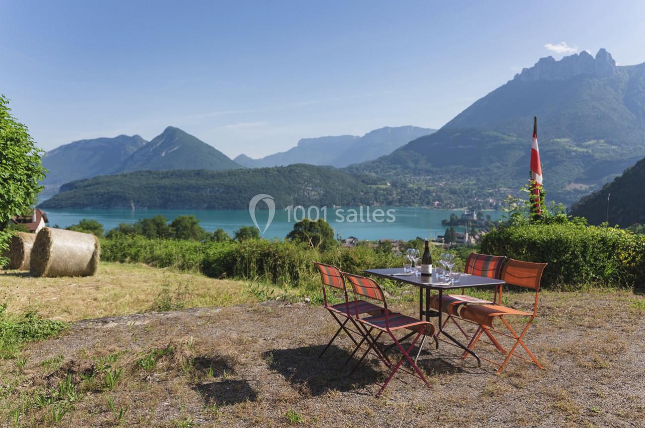 Table et chaises colorées en plein air avec vue sur un lac entouré de montagnes sous un ciel dégagé.