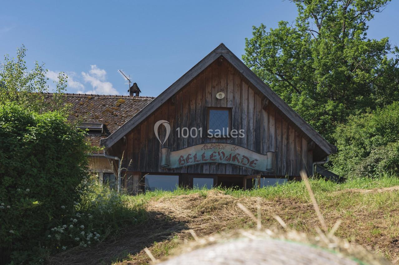 Façade en bois d'une maison rurale entourée de végétation sous un ciel bleu.