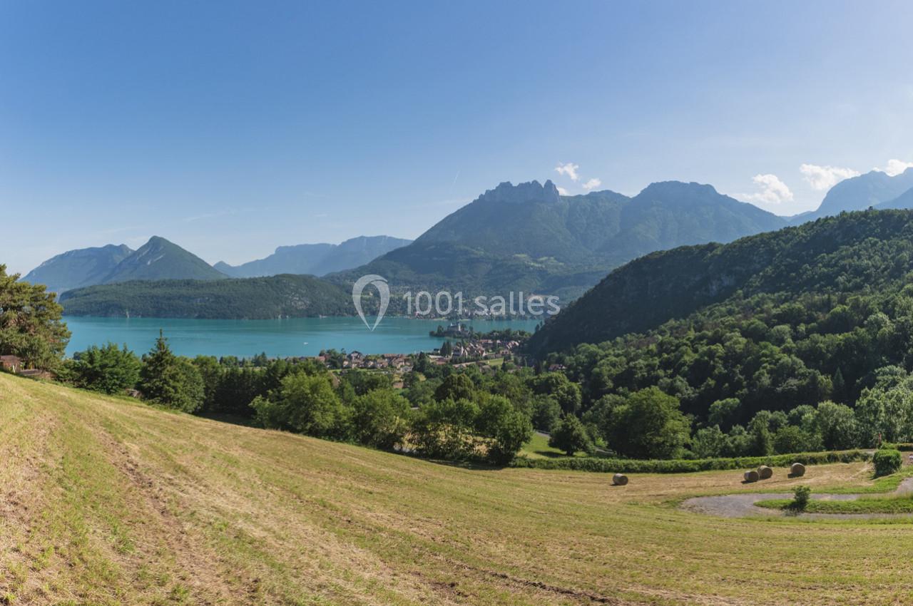 Paysage lacustre avec montagnes en arrière-plan, prairies verdoyantes et village au bord de l'eau sous un ciel dégagé.