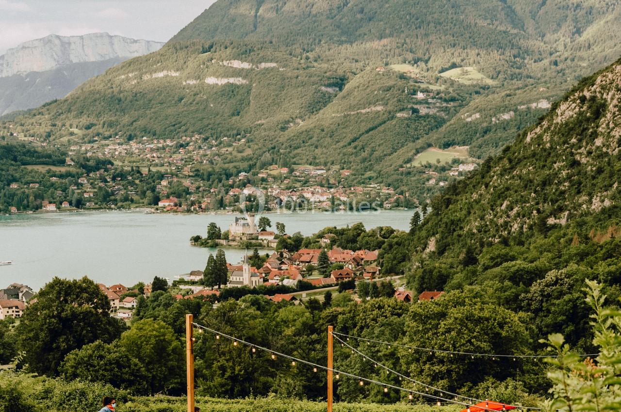 Vue sur un lac entouré de montagnes, avec des tables en plein air et des personnes profitant du paysage.