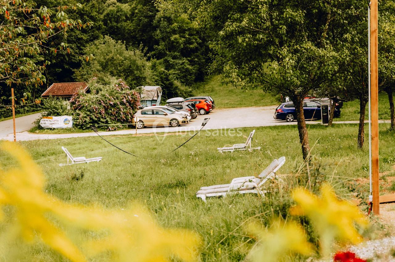Des chaises longues blanches disposées sur une pelouse verdoyante près d'un parking entouré d'arbres.