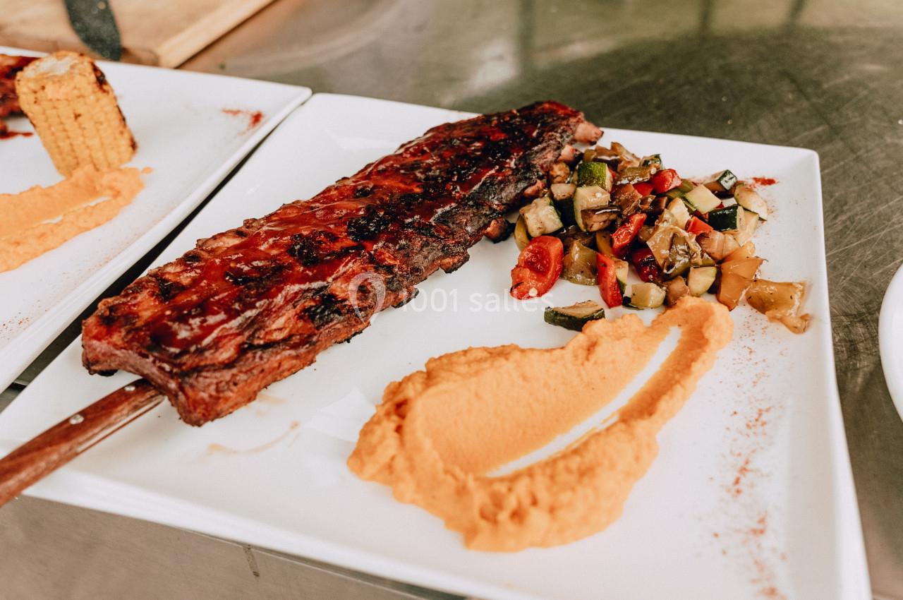 Assiette contenant des côtes grillées, une purée orange et une poêlée de légumes colorés sur une table en métal.