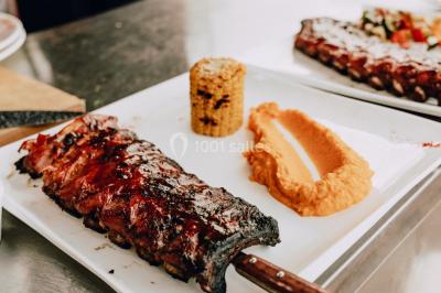 Vue nocturne d'un paysage montagneux avec un village éclairé au loin et une terrasse illuminée au premier plan.