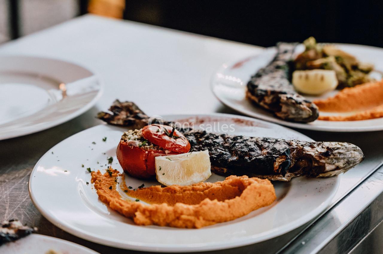 Assiette de poisson grillé avec purée de légumes, tomate rôtie et quartier de citron, servie sur une table.