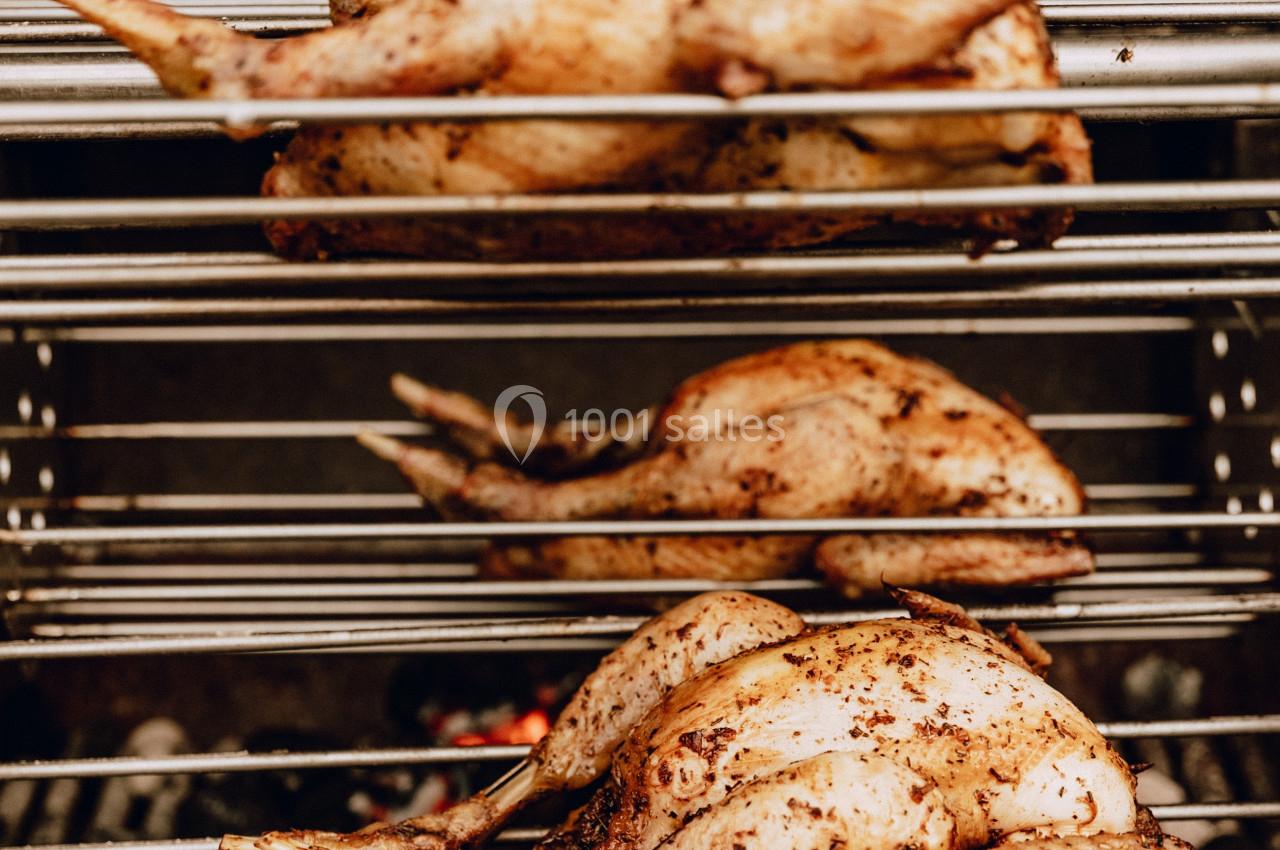 Poulets entiers assaisonnés rôtissant sur des broches au-dessus de braises dans un grill.