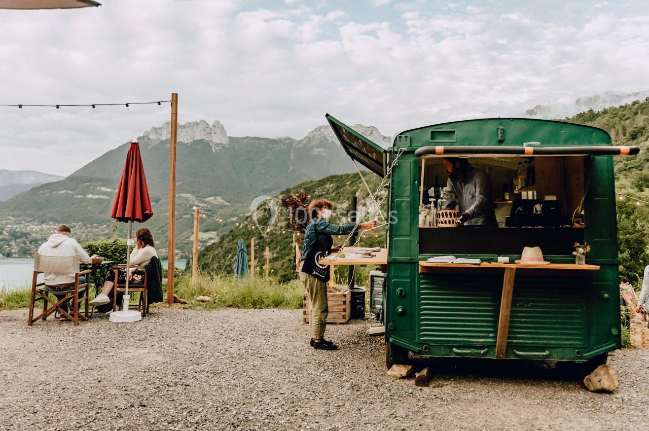 Camion-restaurant vert en plein air avec des clients assis et un paysage de montagnes en arrière-plan.