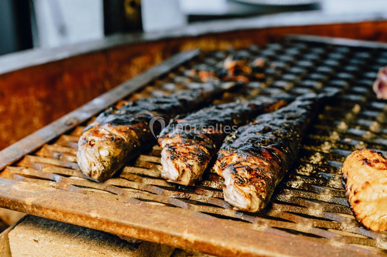 Poissons grillés sur une grille de barbecue, partiellement carbonisés, en cours de cuisson.