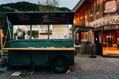 Vue nocturne d'un paysage montagneux avec un village éclairé au loin et une terrasse illuminée au premier plan.