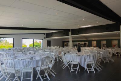 Salon avec fauteuils en cuir, table basse en bois, plante verte, bibliothèque et tableau sur un mur lambrissé.