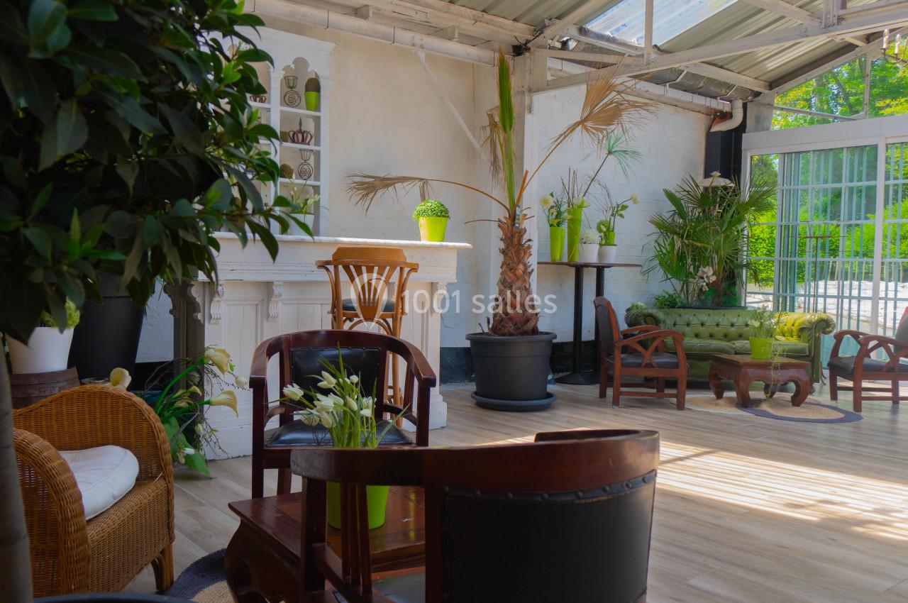 Espace lumineux avec mobilier en bois, plantes vertes et grandes baies vitrées donnant sur un extérieur verdoyant.