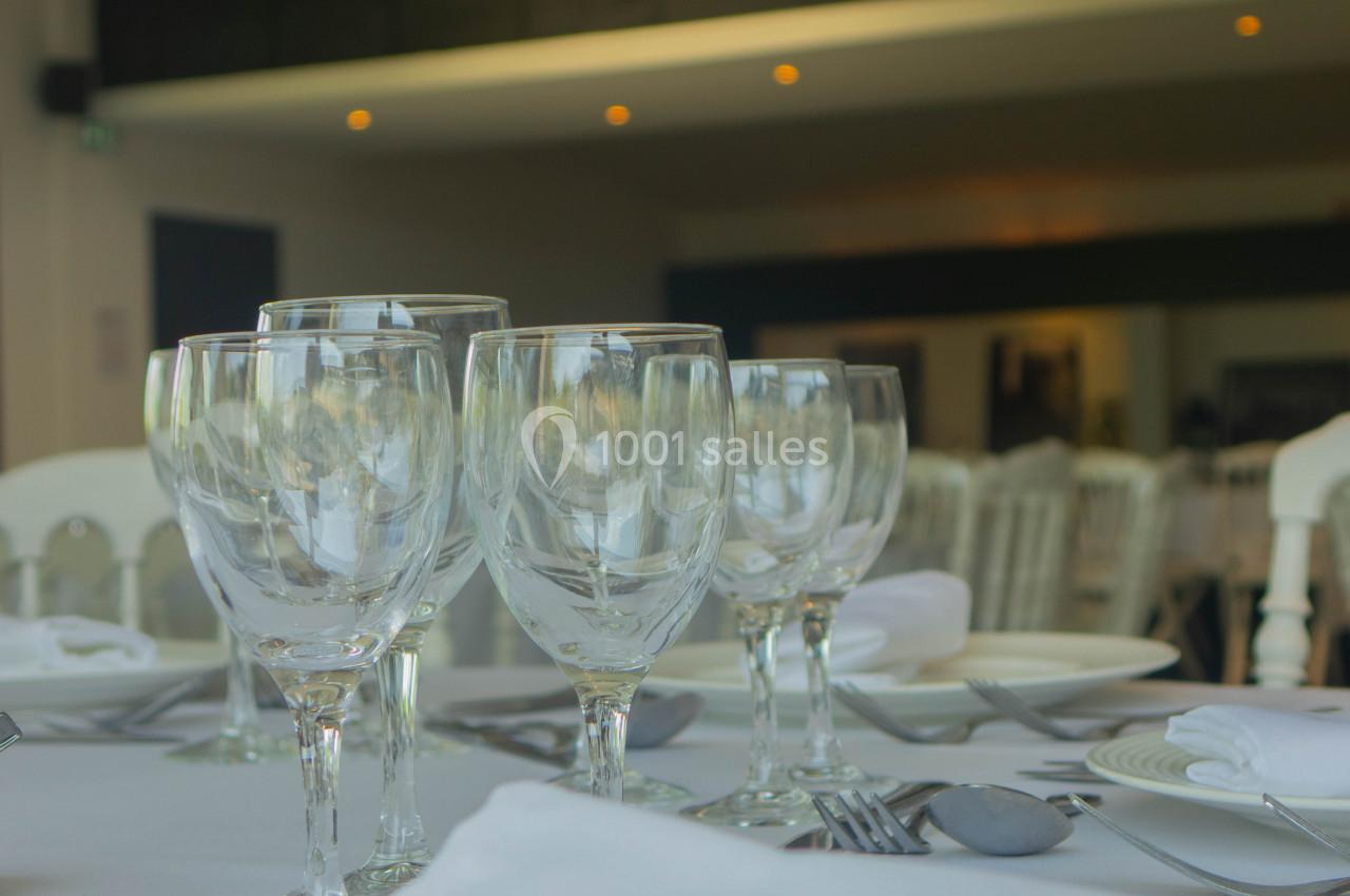 Table dressée avec des verres à pied, assiettes blanches et serviettes, dans une salle lumineuse au décor sobre.