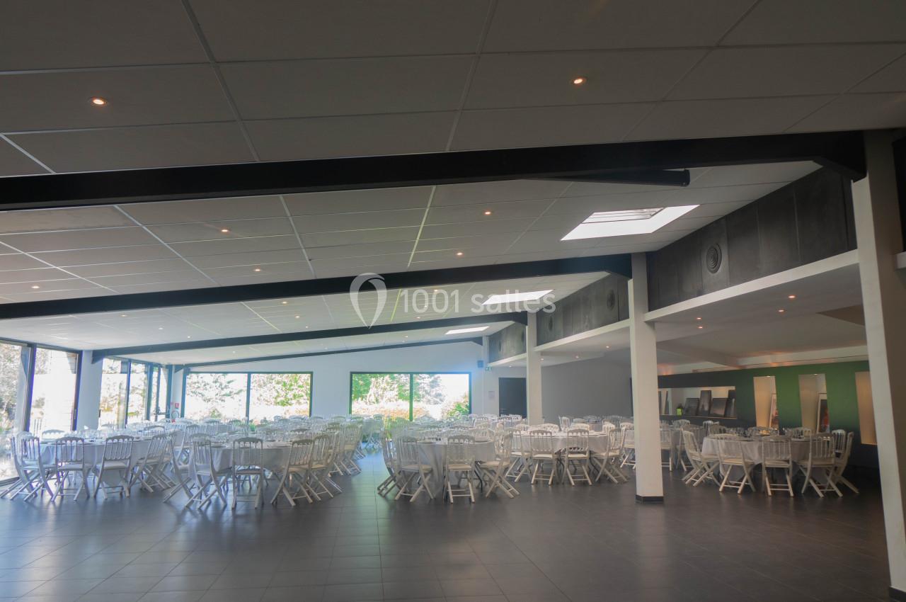 Salle spacieuse avec des tables rondes et des chaises blanches, éclairée par de grandes baies vitrées.