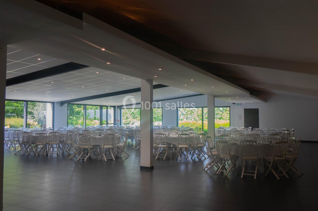 Salle de réception lumineuse avec tables rondes dressées et grandes baies vitrées donnant sur un jardin.