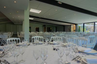 Salon avec fauteuils en cuir, table basse en bois, plante verte, bibliothèque et tableau sur un mur lambrissé.