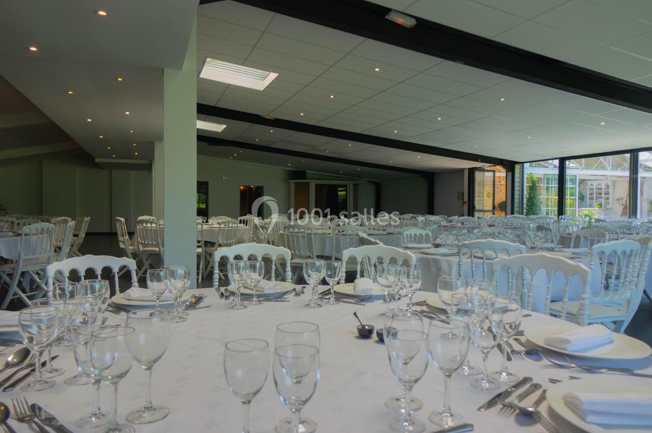 Salle de réception lumineuse avec tables dressées, nappes blanches, verres et couverts, prête pour un événement.